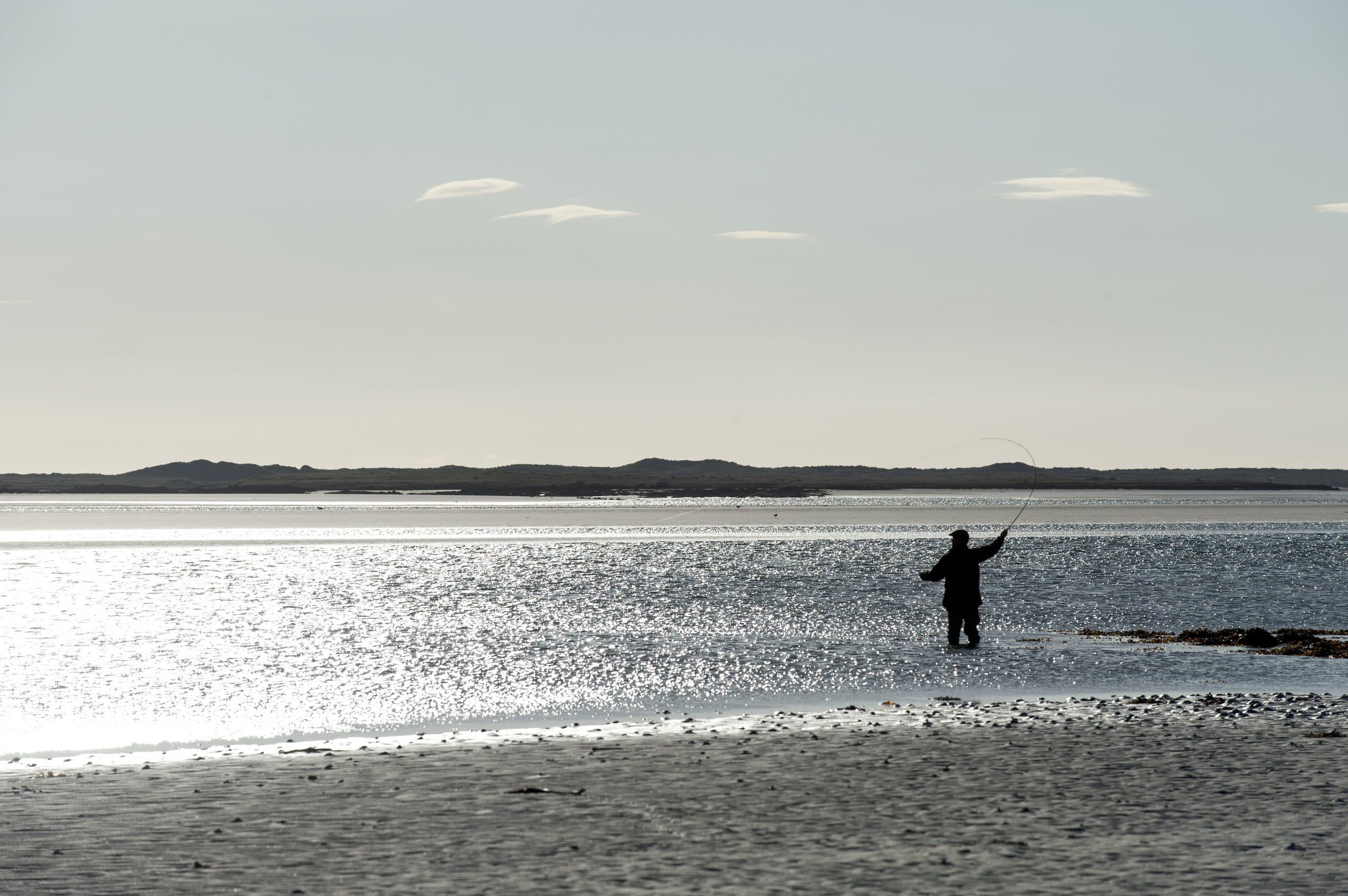An angler wading a sea pool on North Uist, the water lit silver