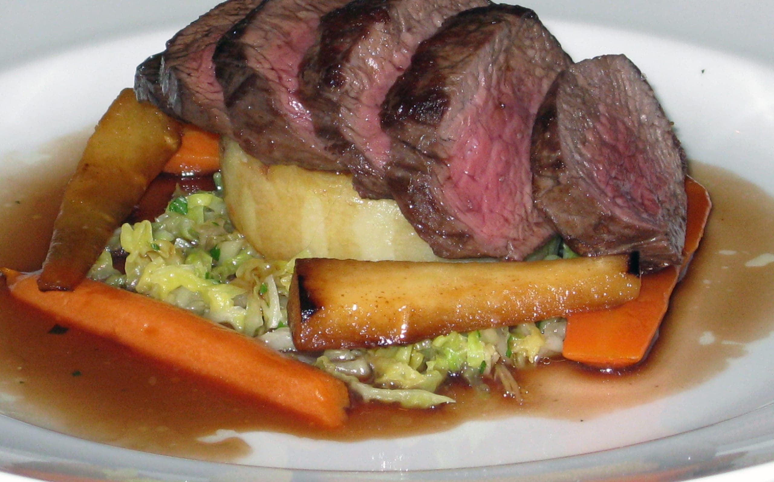 Sliced pink venison loin with roast parsnips, carrots and cabbage